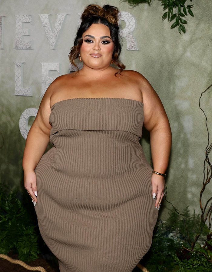 Plus size woman in a strapless brown dress posing at an event, former body positivity influencer discussing movement views.