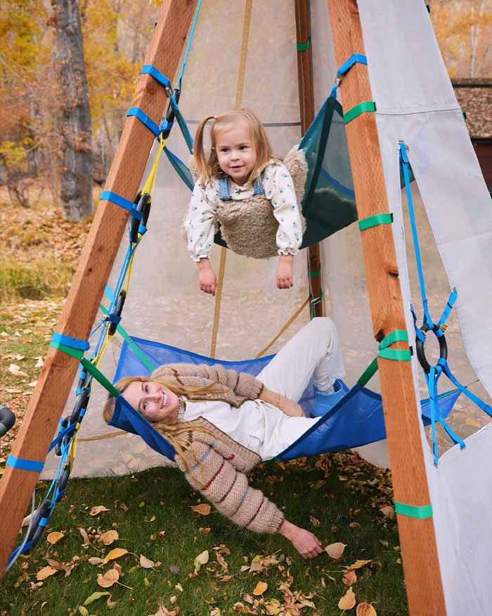 Young woman relaxing on a hammock with a child playing above, illustrating Rumer Willis working four jobs despite famous parents.