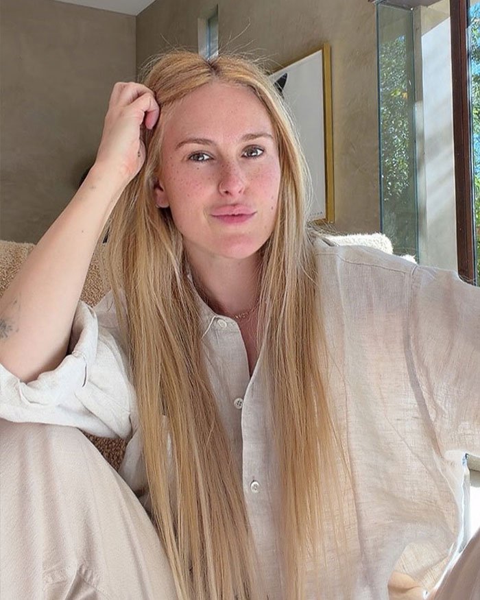 Rumer Willis sitting indoors in casual beige outfit, sharing her experience working four jobs despite famous parents.