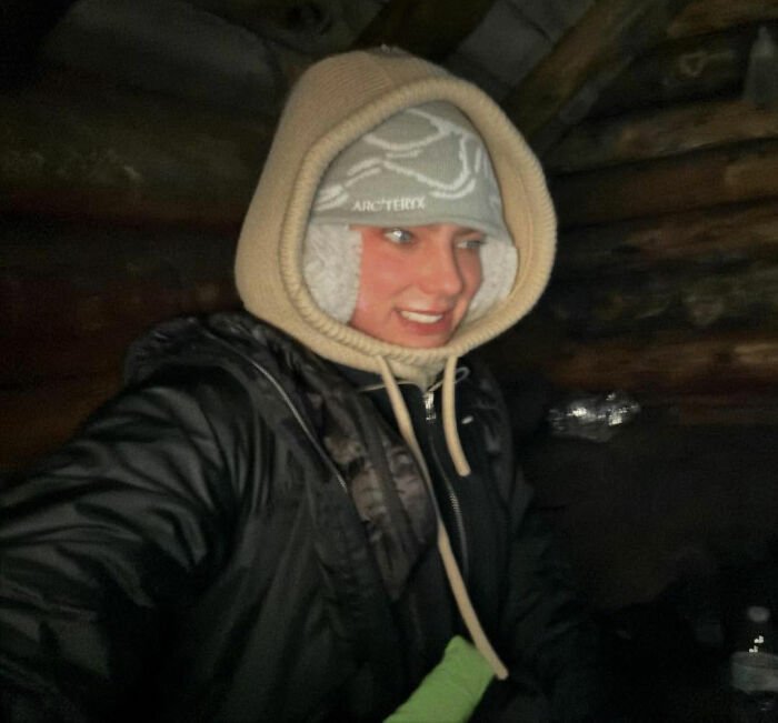 Young woman hiking New York's highest peak with her dog, dressed warmly in a black jacket and hooded hat indoors.