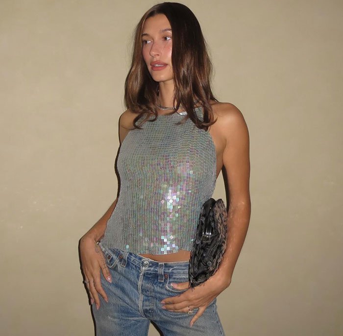 Hailey Bieber posing in a sequin top and jeans, amid discussions of pathological liar claims about her toddler son.