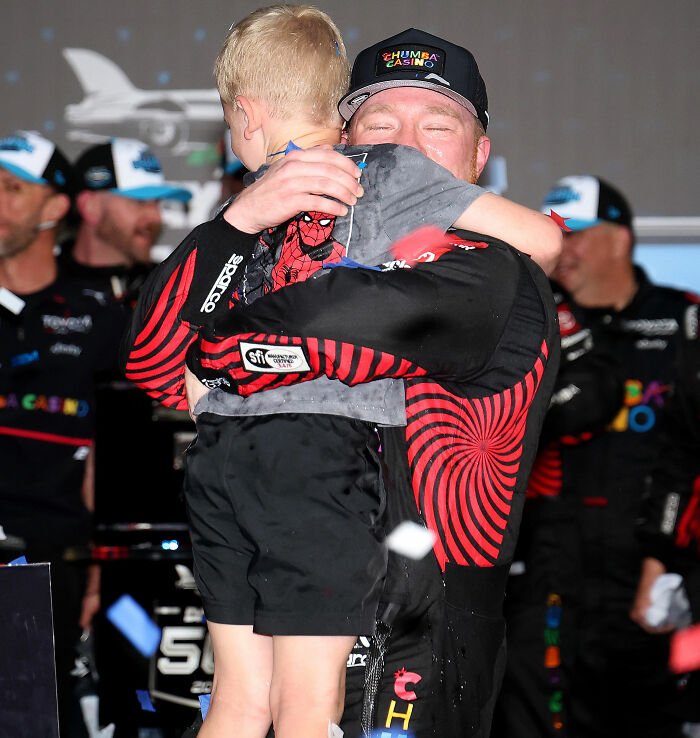 NASCAR driver hugging his young son during post-race celebration after Michael Jordan interaction controversy.