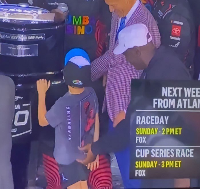 NASCAR driver interacting with a child while discussing Michael Jordan and controversy in a racing event setting.