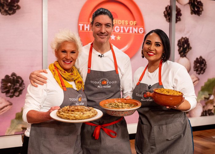 Three chefs wearing aprons holding dishes in a cooking show kitchen, related to police report and tragic passing news.