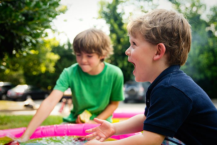 Two young boys playing near a small pool outdoors, capturing a playful moment related to kids and family life.