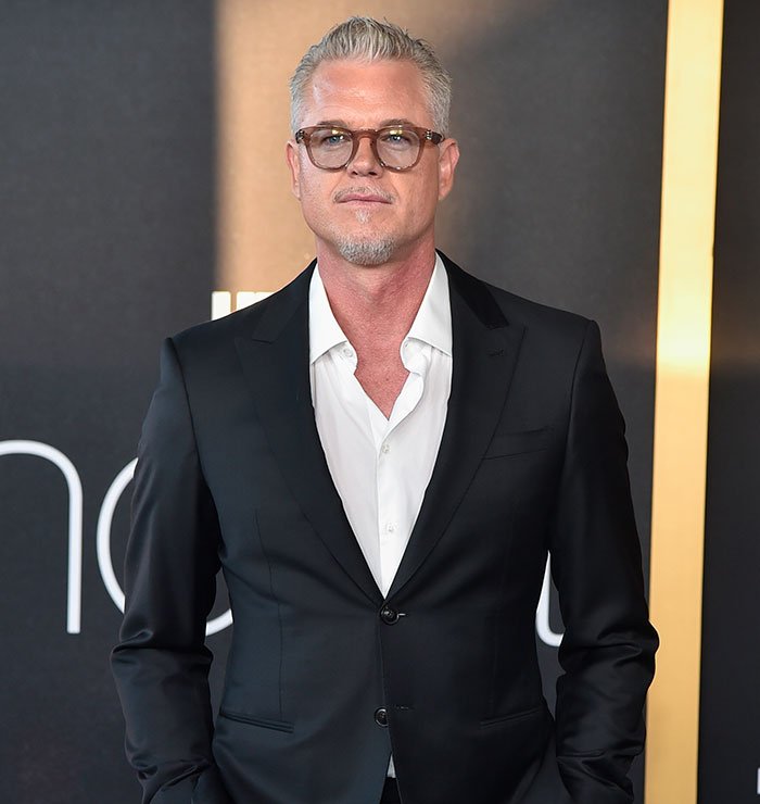 Man in a black suit and glasses standing against a dark background, representing doctors breaking down ALS symptoms.