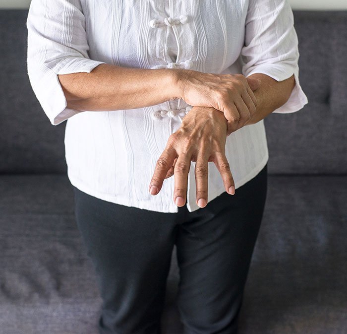 Person in white shirt holding wrist, illustrating commonly ignored ALS symptoms related to hand and muscle issues.