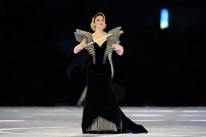 Female Winter Olympics host in an elegant black dress conducting an event before resigning after commentary sparked outrage.