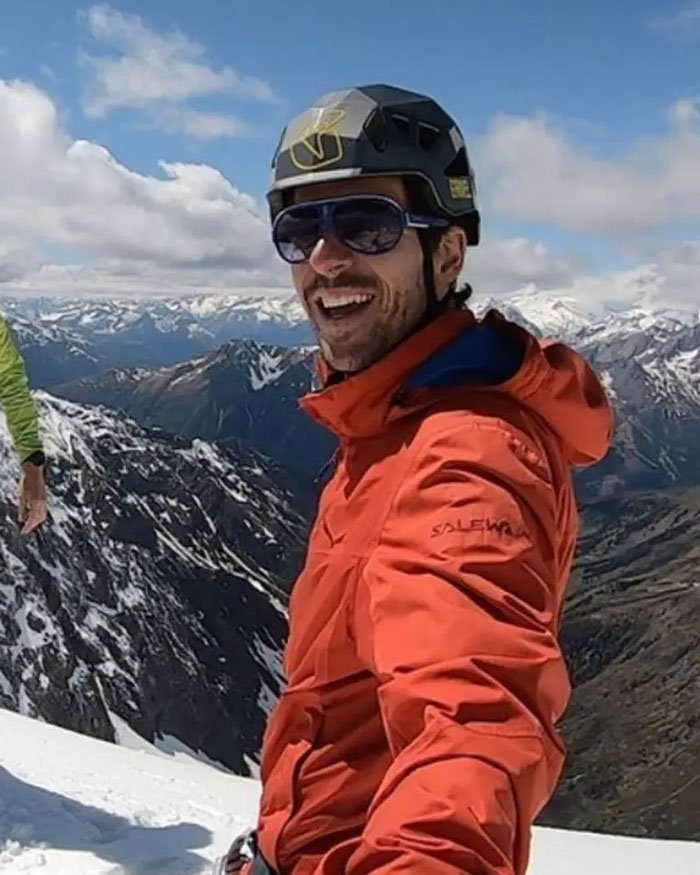 Climber wearing helmet and sunglasses on snowy mountain with scenic valley in background, revealing heartbreaking last words.