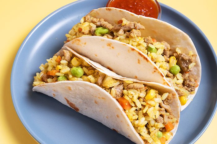 Two tacos filled with rice, vegetables, and meat on a blue plate, highlighting challenges eating with throat pain.