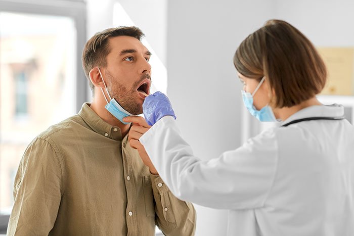 Doctor wearing gloves examines man’s throat, addressing years of persistent throat pain and medical mystery.