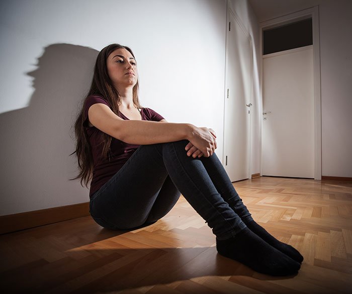 Young woman sitting on floor looking upset and reflective, illustrating man can&rsquo;t handle girlfriend doing maid of honor duties.