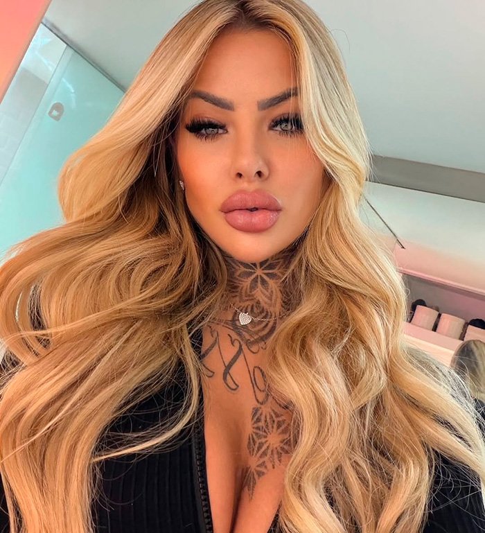 Glamorous influencer with long blonde hair and tattoos, highlighting major plastic surgery complications at age 27.