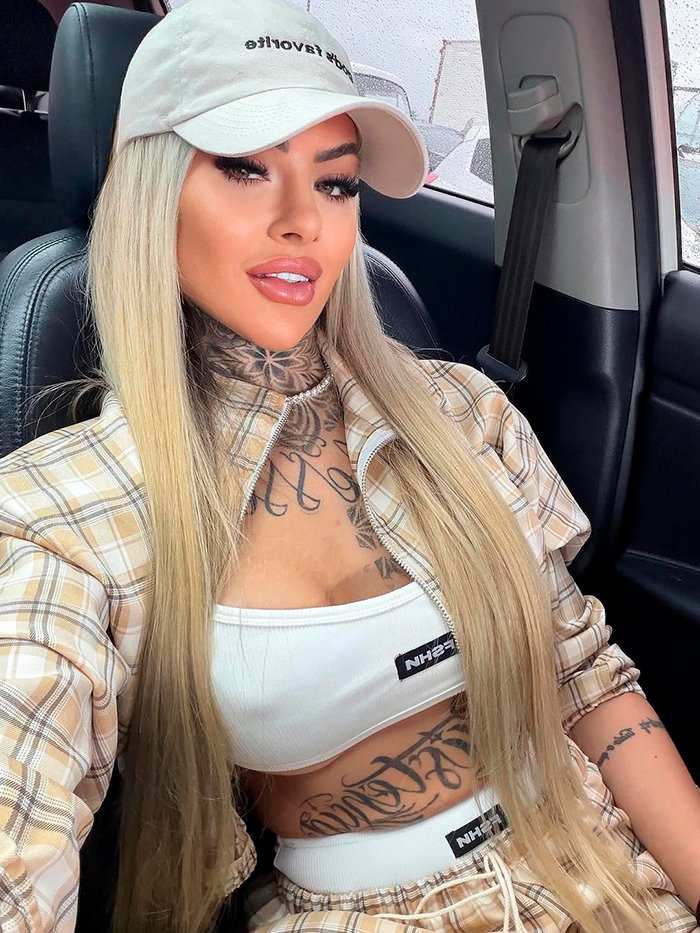 Glamorous influencer with long blonde hair and tattoos taking a selfie in a car following plastic surgery complications.