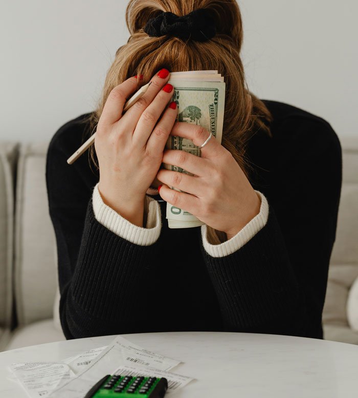 Woman holding cash and covering her face, symbolizing secrets and financial concerns in a relationship before wedding call-off.