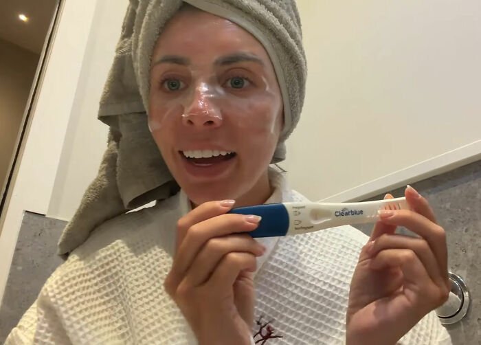 Woman with towel on head showing positive pregnancy test, related to Bonnie Blue pregnancy and 400-men challenge.