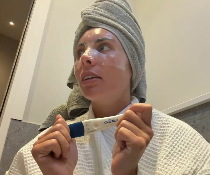Bonnie Blue in a bathrobe and towel holding a positive pregnancy test after a 400-men challenge announcement.