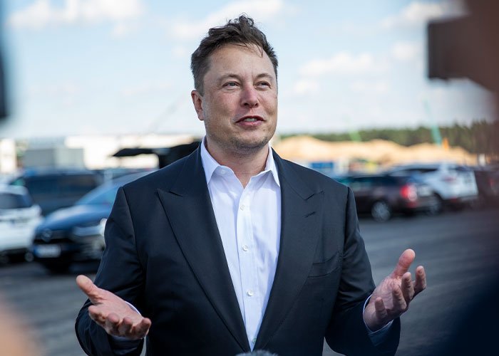Elon Musk speaking outdoors in a suit and white shirt, sparking theories about something really bad coming.