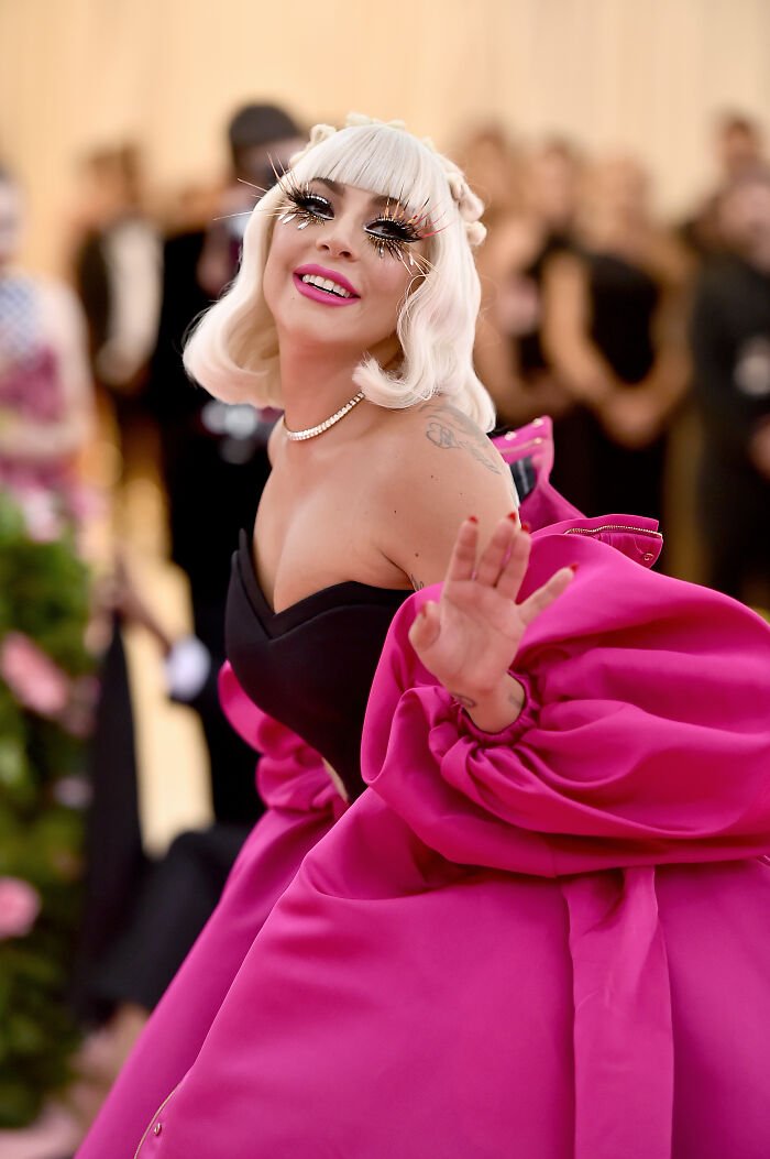 A glamorous woman at the Met Gala wearing a dramatic pink gown and bold eyelashes, highlighting the 2026 dress code controversy.