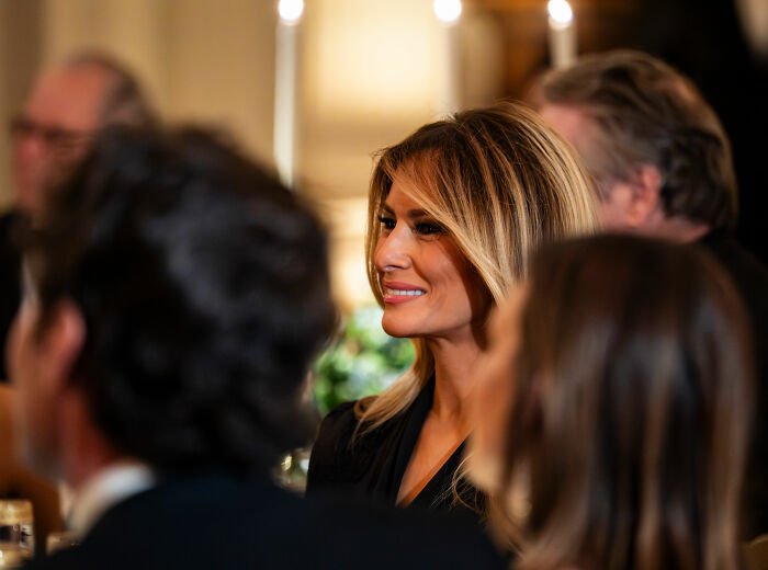 Melania Trump attending a governors dinner, smiling and dressed in a black outfit amid a formal gathering.