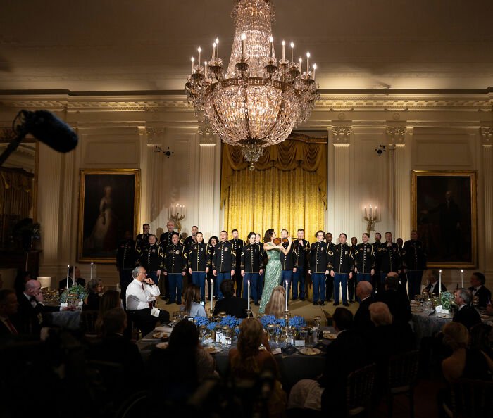 Military band performs at an elegant governors dinner event with Melania Trump's controversial outfit in the background.