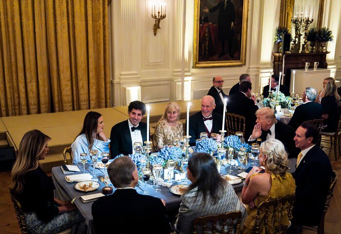 Melania Trump at a governors dinner, wearing a light blue outfit, seated among guests in a formal dining setting.