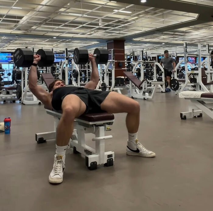 Man lifting dumbbells on bench in gym, symbolizing Canadian hockey fans' bold Olympic bet after USA wins gold.