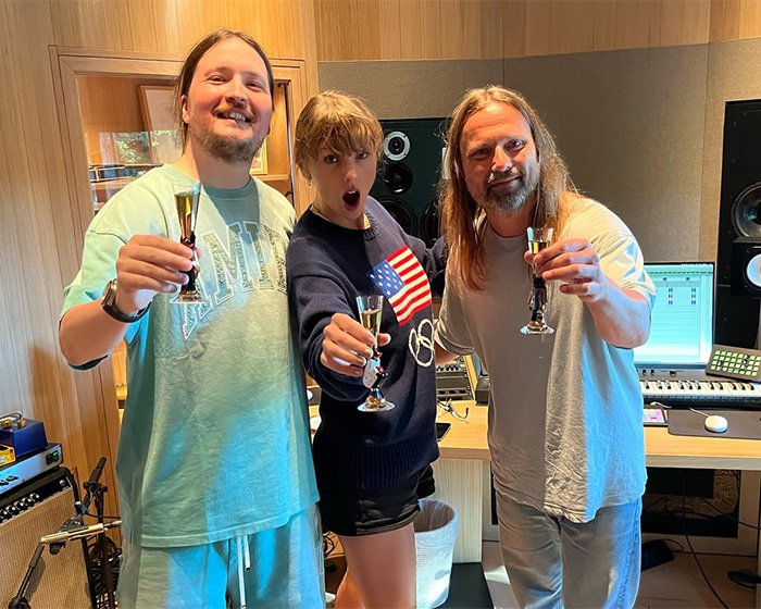 Taylor Swift makeup-free in a behind-the-scenes video with colleagues, celebrating in a music studio environment.