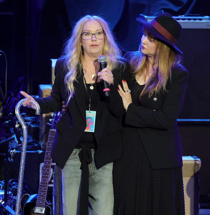 Christina Applegate speaking on stage with a microphone, sharing an emotional multiple sclerosis battle update.
