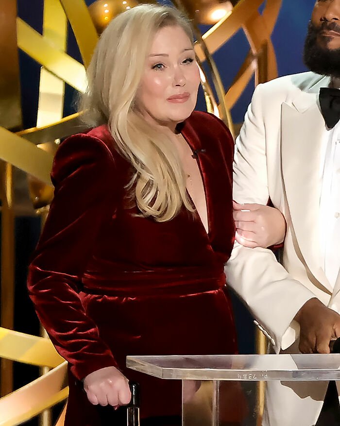Christina Applegate wearing a red dress, using a cane, sharing an update on her battle with multiple sclerosis at an event.