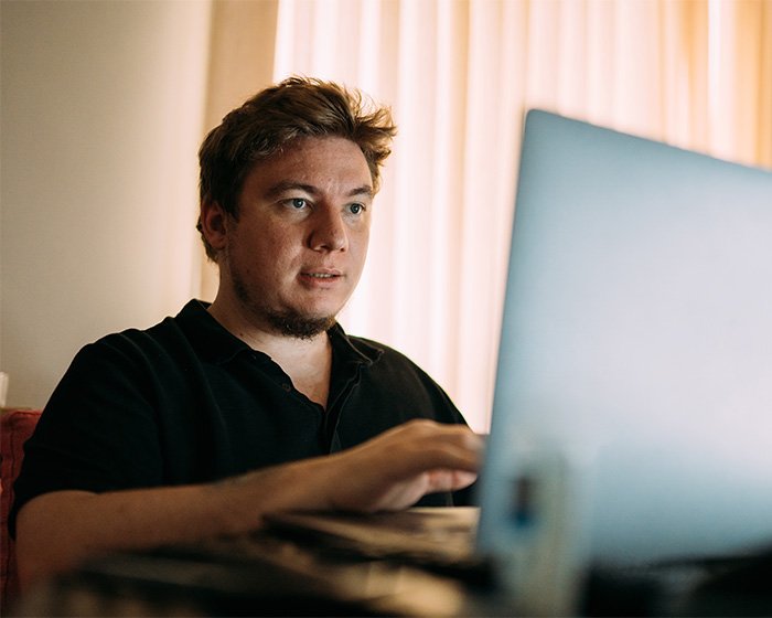 Young man focused on laptop screen, representing discovery of boyfriend’s YouTube history and woman's danger awareness.