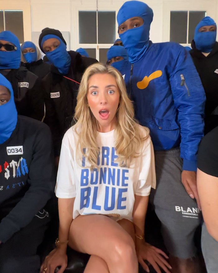 Participant from Bonnie Blue’s 400-Men Challenge with surprised expression surrounded by men in blue masks and black outfits.