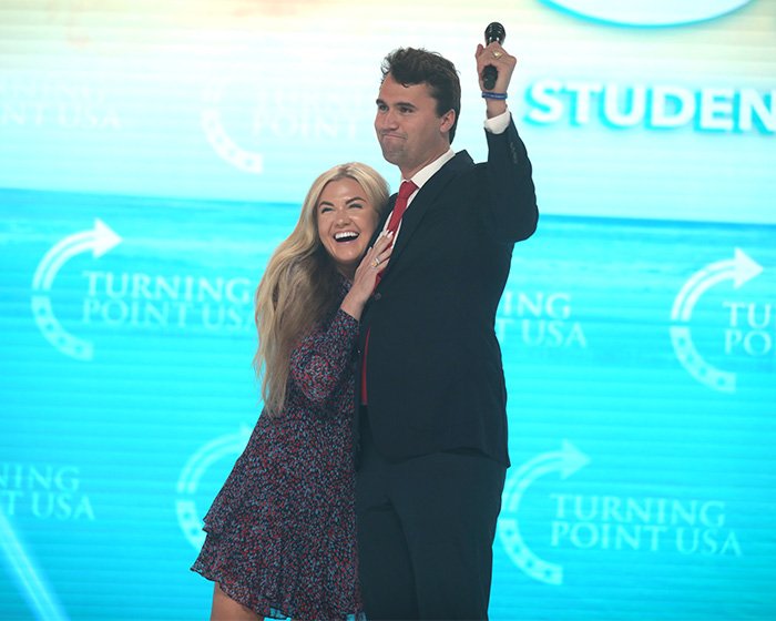 Erika Kirk smiling and hugging a man on stage at a Turning Point USA event, going viral for her reaction to Trump.