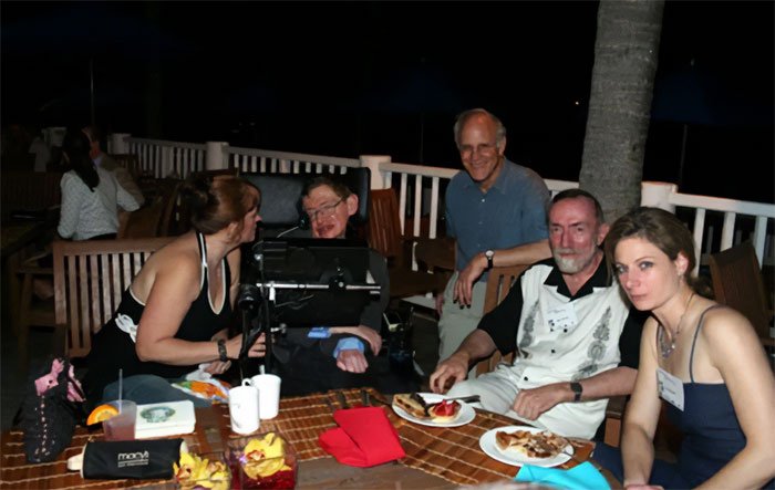 Stephen Hawking with family and friends seated at a table outdoors, related to Epstein files and comic reactions.