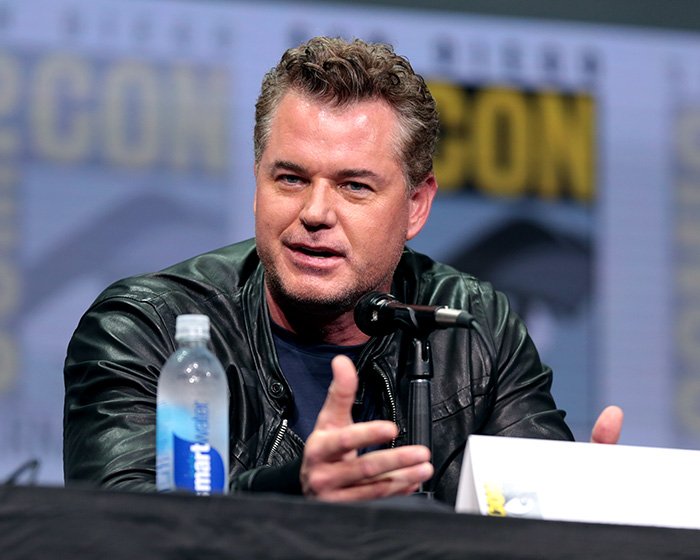 Eric Dane speaking at a panel event, wearing a black leather jacket, discussing his scandalous lifestyle and downward spiral.