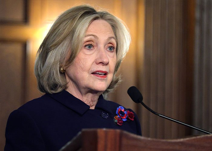 Hillary Clinton speaking at a podium during a congressional clash, addressing Epstein claims involving Trump and Bill Clinton.