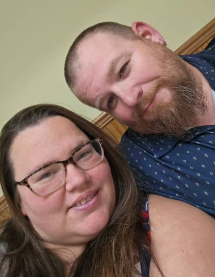 Heartbroken mom of 11-year-old and bearded man sitting close together, sharing a quiet moment indoors.