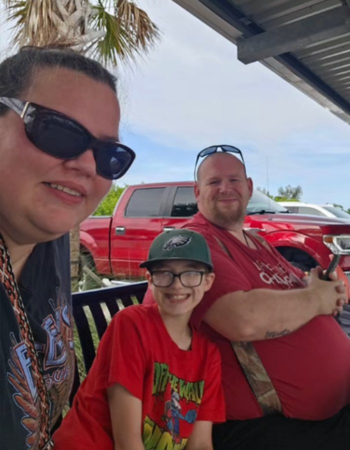 Heartbroken mom with her 11-year-old child and adoptive father sitting outdoors by a red truck.