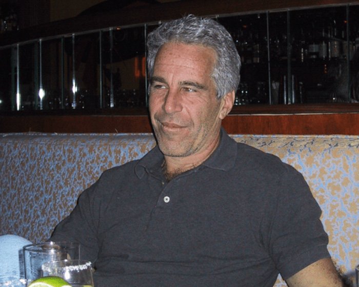 Man with gray hair wearing a black polo shirt seated in a booth with drinks, related to Clinton statement on Epstein ties.