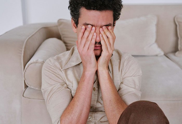 Man sitting on couch covering face with hands, reflecting emotions after giving wife a second chance.