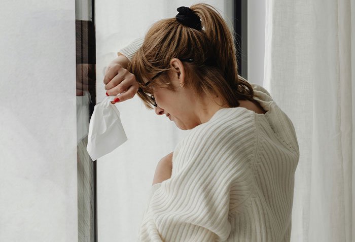 Woman holding tissue by window, emotional and crying, representing a wife seeking a second chance from her husband.