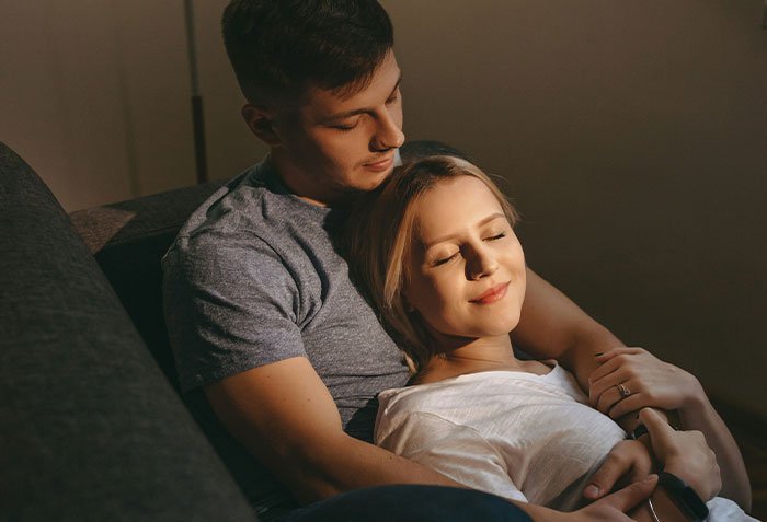 Man gives wife a second chance as they embrace on a couch, showing forgiveness and renewed relationship connection.