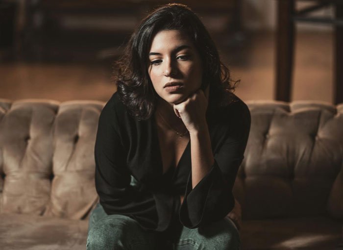 Young woman fed up with being roommates&rsquo; personal doorman, sitting on couch looking frustrated and ignoring calls.