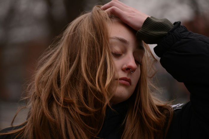 Young woman with nose rings touching her hair, looking pensive outdoors, expressing feelings about moving in and apartment issues.
