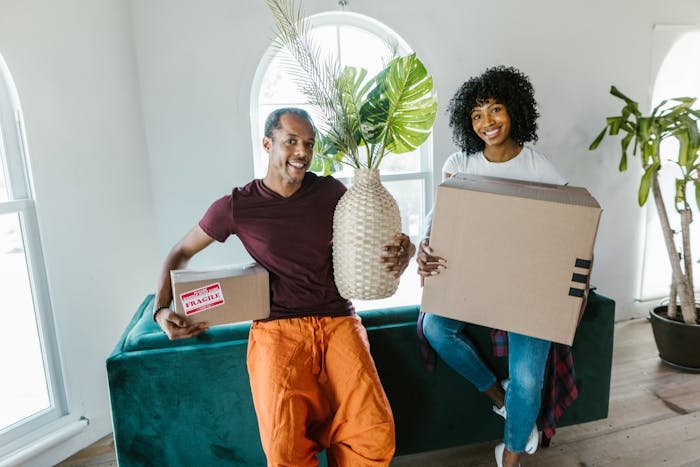 Couple moving in together, man holding fragile box and vase, highlighting apartment living and relationship challenges.