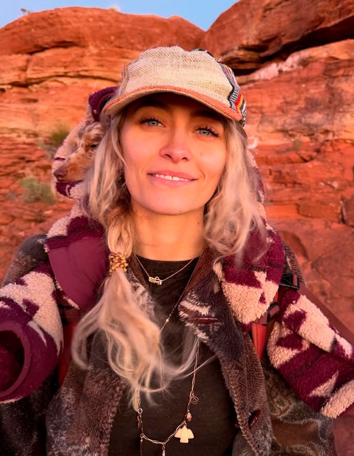 Young woman wearing a patterned jacket and cap outdoors with red rock background, related to biological dad fan scrutiny topic.