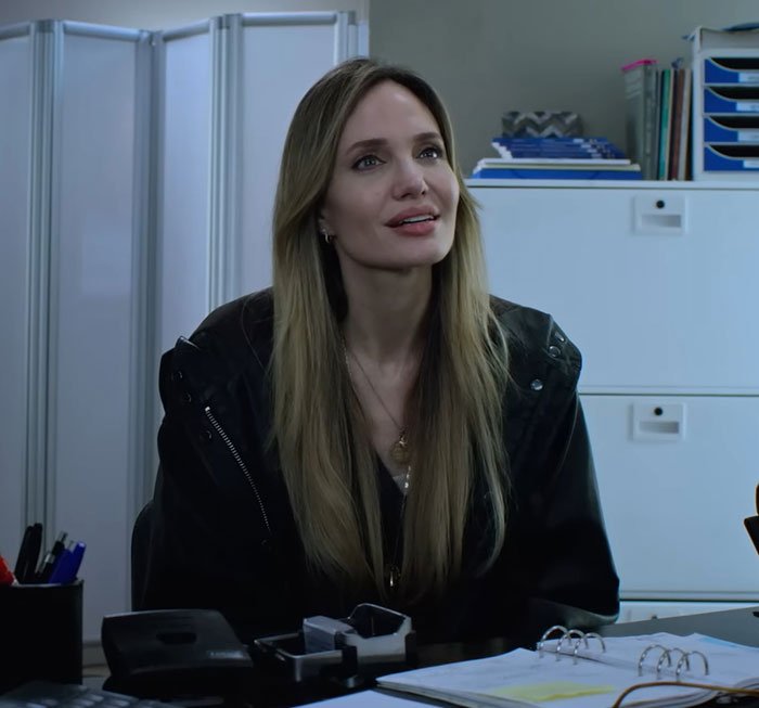 Woman with long hair wearing a black jacket sitting at a desk conveying Brad Pitt's kids relationship message in movie.