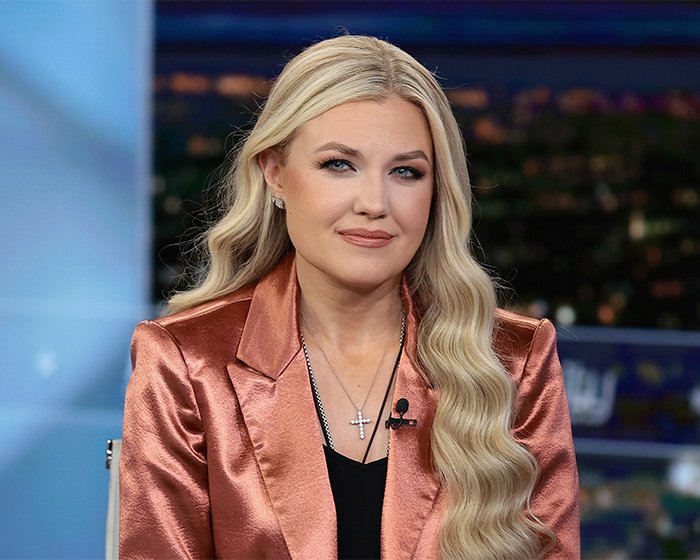 Erika Kirk in a shiny copper blazer, sitting in a studio setting with soft waves and subtle makeup.