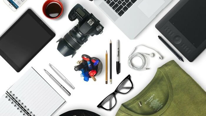 Flat lay of items including camera, laptop, tablet, glasses, pens, and t-shirt to challenge naming objects quiz