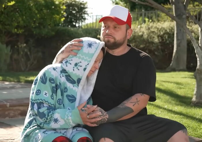 Couple sitting outside, comforting each other after discovering roommate’s horrifying acts on security footage.
